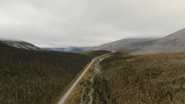 View of Scenic Road from Above surrounded by Mountains and Forest on a Cloudy Fall Day. Aerial Drone Shot. Taken near the Dempster Highway, Yukon, Canada.
