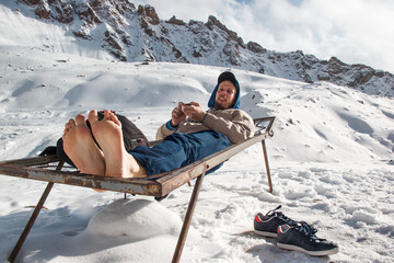 A man in winter with barefoot feet is resting on an iron bed in the mountains. Winter vacation fun...