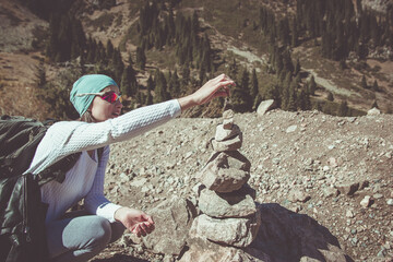A young woman in glasses builds a pyramid of stones. Stones in the background of trees.