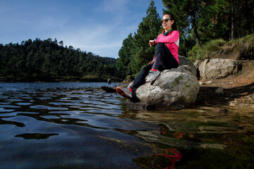 Atleta descansando a la orilla de un lago sentada sobre una piedra, después de correr en el bosque.