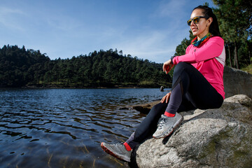 Atleta descansando a la orilla de un lago sentada sobre una piedra, después de correr en el bosque.