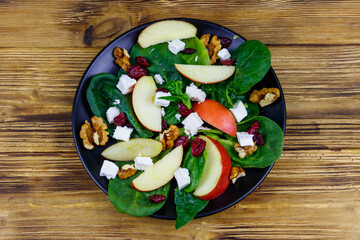Autumn spinach salad with apple, feta cheese, walnut and dried cranberry on wooden table. Top view. Healthy vegetarian food