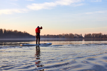 Water tourists is paddling on SUP (Stand up paddle board) at Danube river at cold season. Concept of water tourism, healthy lifestyle and recreation at winter