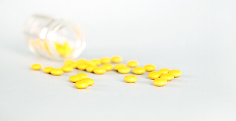 Yellow tablets from a glass jar are scattered against a light background.