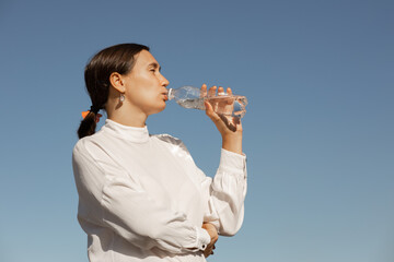 Woman in white blouse drinks water against blue sky