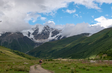 Fototapeta na wymiar Hikers on a hiking trail in with snow-capped mountain range on the background, the Caucasus Mountains, Svaneti, Georgia.