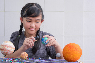 Selective focus at young Asian girl making homemade solar system model on wooden table at home for her science homework project at school © Prapat