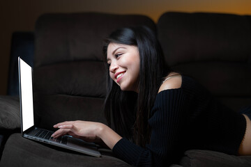 Young woman smiling in front of the computer resting on a sofa

