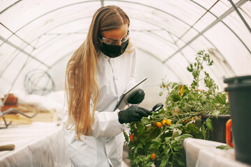 A woman scientist in a white coat and glasses examines a sample of a plant through a magnifying...