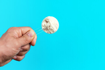 Male hand holds a scoop with protein on blue background top view.