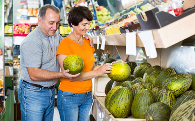 Fototapeta premium Nice man and his wife are choosing ripe melon in the fruit store