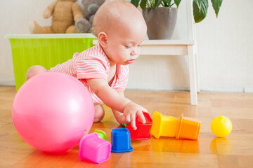 Little baby girl sitting on the floor, crawling and playing with brightly colored educational toys