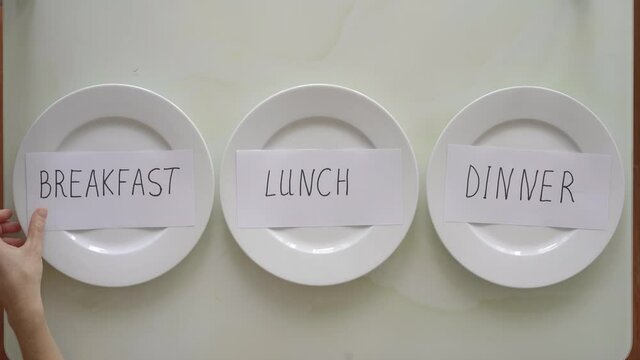 A woman replaces inscriptions breakfast, lunch, and dinner on empty plates with inscriptions fasting. Interval fasting concept. Skipping meals