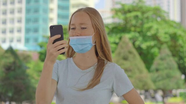 On a street a young woman talks to a phone wearing medical face mask in the wrong way. Her mask does not cover her nose. Wrong-way of using a face mask