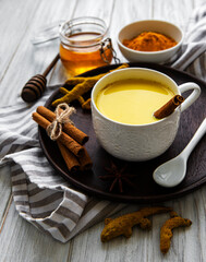 Yellow turmeric latte drink. Golden milk with cinnamon, turmeric, ginger  and honey over white wooden background.