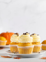 Pumpkin cupcakes (orange muffins with cream cheese frosting) decorated with chocolate sprinkles. Seasonal autumn dessert, fall background, maple leaves. Concrete background, copy space, close up view.