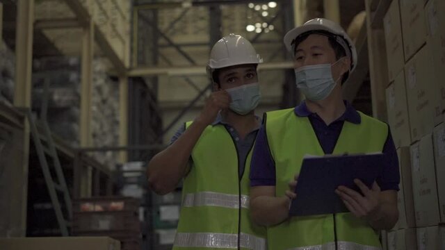 Group of young factory warehouse workers wearing a protective face mask while working in logistic industry indoor. Asian and Indian ethnic men checking item order - Front View - HD Slow Motion Footage