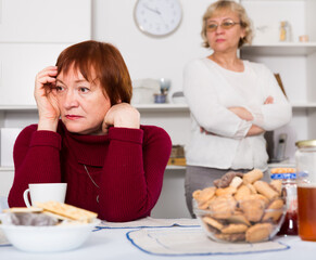 Pensioners females quarreling at kitchen near food at the table