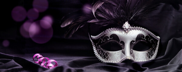 venetian mask with feather on dark fabric with purple blur light and ribbon