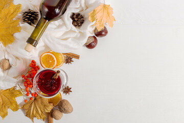 A cup of mulled wine with spices, bottle, scarf, spices, dry leaves and oranges on the table....