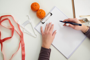 Nutritionist doctor writing diet plan on table with measuring tape, view from above