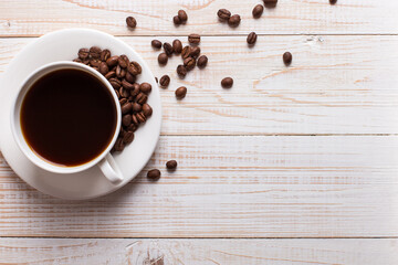 Cup of coffee with scattered coffee beans on a wooden table background. Autumn morning mood, copy space.