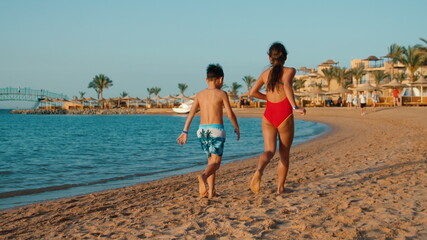 Barefoot children having fun at seashore in sunset. Sibling running on sea beach