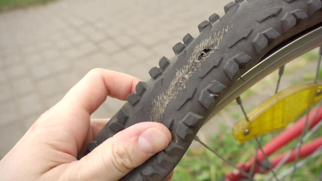 A cyclist inspects an old punctured tire on a bicycle wheel, outdoor