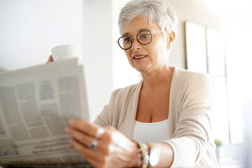 portrait of a beautiful 55 year old woman with white hair reading a newspaper