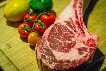 a slab of raw marbled beef steak with tomatoes on a wooden block