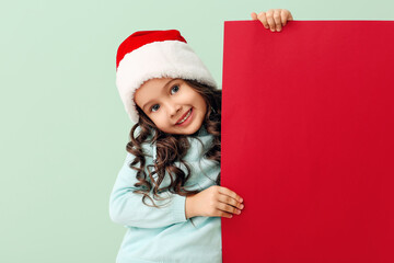 Cute little girl in Santa hat and with poster on color background