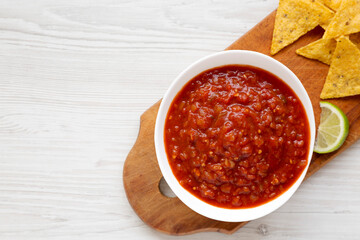 Homemade Tomato Salsa and Nachos on a rustic wooden board on a white wooden table, top view. Flat lay, overhead, from above. Space for text.