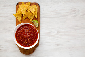 Homemade Tomato Salsa and Nachos on a rustic wooden board on a white wooden background, top view....