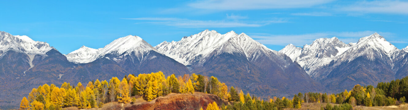 A panoramic view of the snow-capped peaks of the Eastern Sayan mountain range on a sunny autumn day. Siberia, Buryatia, Tunka foothill valley. Beautiful autumn landscape. Natural background