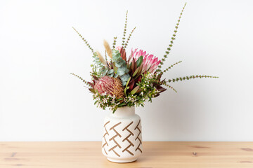 Stylish Australian native floral arrangement of a red protea flower, orange and red banksias, red...
