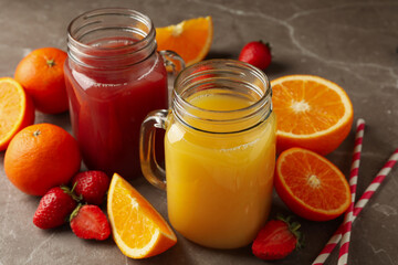 Glass jars with strawberry and orange juices on gray background