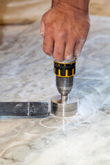 handyman cut round holes for electrical outlets in the marble countertop for the kitchen using a hand drill
