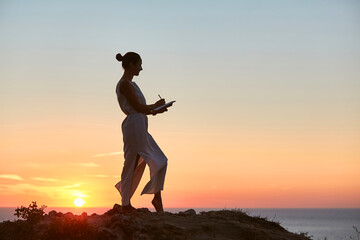 Lady writing in personal notebook on sunset. Virgin nature and time alone idea. Keeping diary and contemplation concept