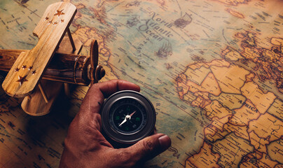 Hand hold old compass discovery and wooden plane on vintage paper antique world map background,...