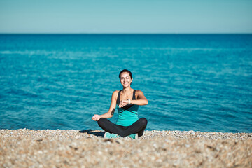 Fototapeta na wymiar Woman sitting on beach and looking on watch. Calm sea and nature. Take care of health. Sport and active lifestyle idea