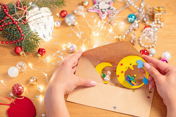 Christmas concept. Human hands put christmas wooden decoration to an envelope,  with festive lights and ornaments on background