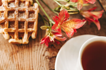 cup of tea and flowers.  alstroemeria and a cup of tea. Viennese waffles on a wooden background. morning breakfast. beautiful still life