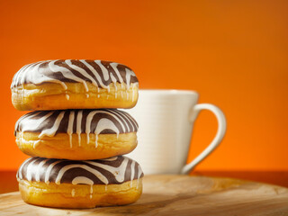 Stack of three doughnut with chocolate and sugar glaze in zebra pattern on a wooden board and table, One white tea cup in the background. Warm sunny background. Bakery product