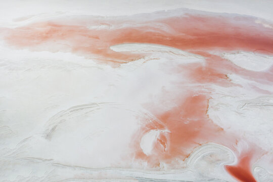 Natural background of the white surface of a salty reservoir with a pink abstract pattern due to algae blooming. Shooting from a drone.