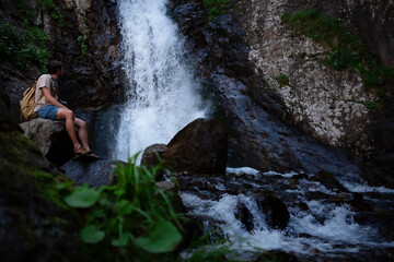Hiker waalkinh with backpack looking at waterfall in park in beautiful nature landscape.