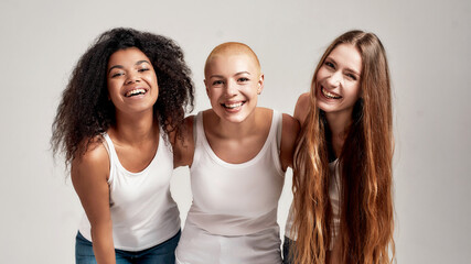 Three confident young diverse women wearing white shirts smiling at camera while posing together...