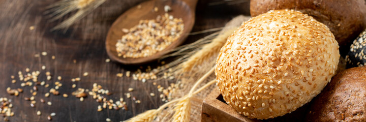 Sesame buns for burgers. Buns in a wooden box on a brown wooden table. Homemade buns with sesame seeds. Baking close-up. Banner with a copyspace