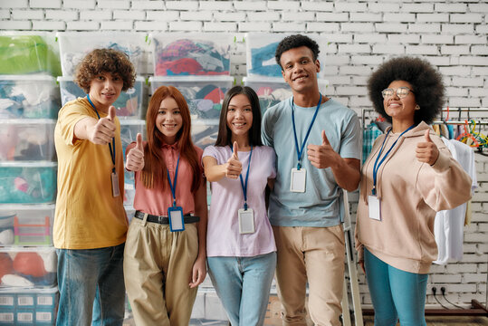 Young and diverse volunteer group smiling at camera, showing thumbs up while posing in front of boxes full of clothes, Happy team working for a charity, donating apparel to needy people