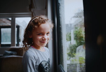 Portrait of smiling school girl standing near window with rain drops on window in rainy season