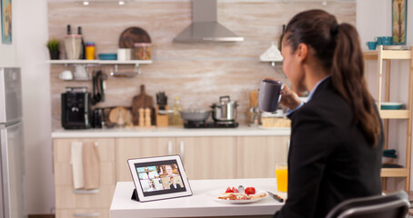 Businesswoman using a tablet for video call during breakfast. Young freelancer in the kitchen talking on a video call with her colleagues from the office, using modern internet technology